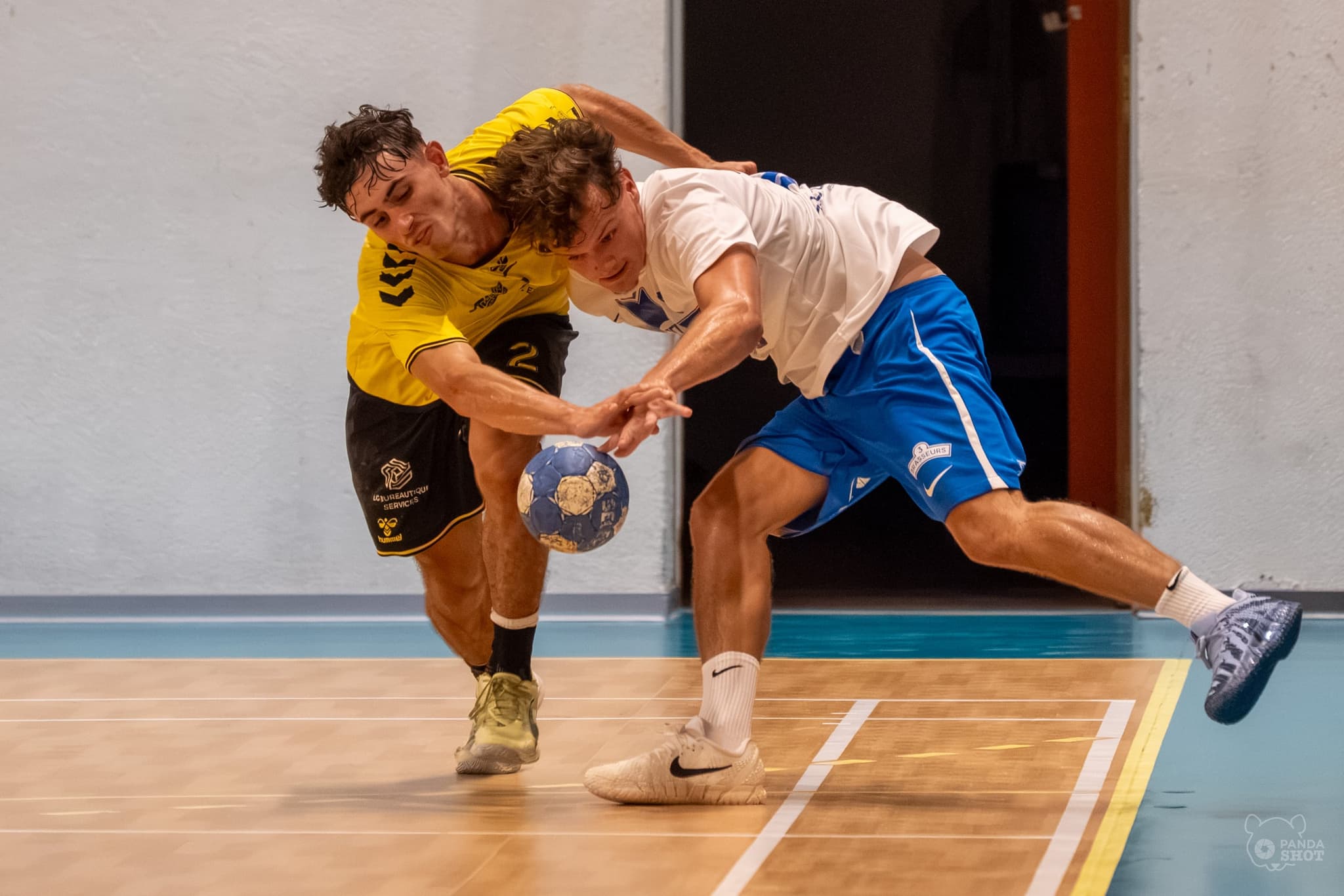 Deux joueurs sprintent vers le ballon et le disputent à hauteur du sol, match de handball masculin