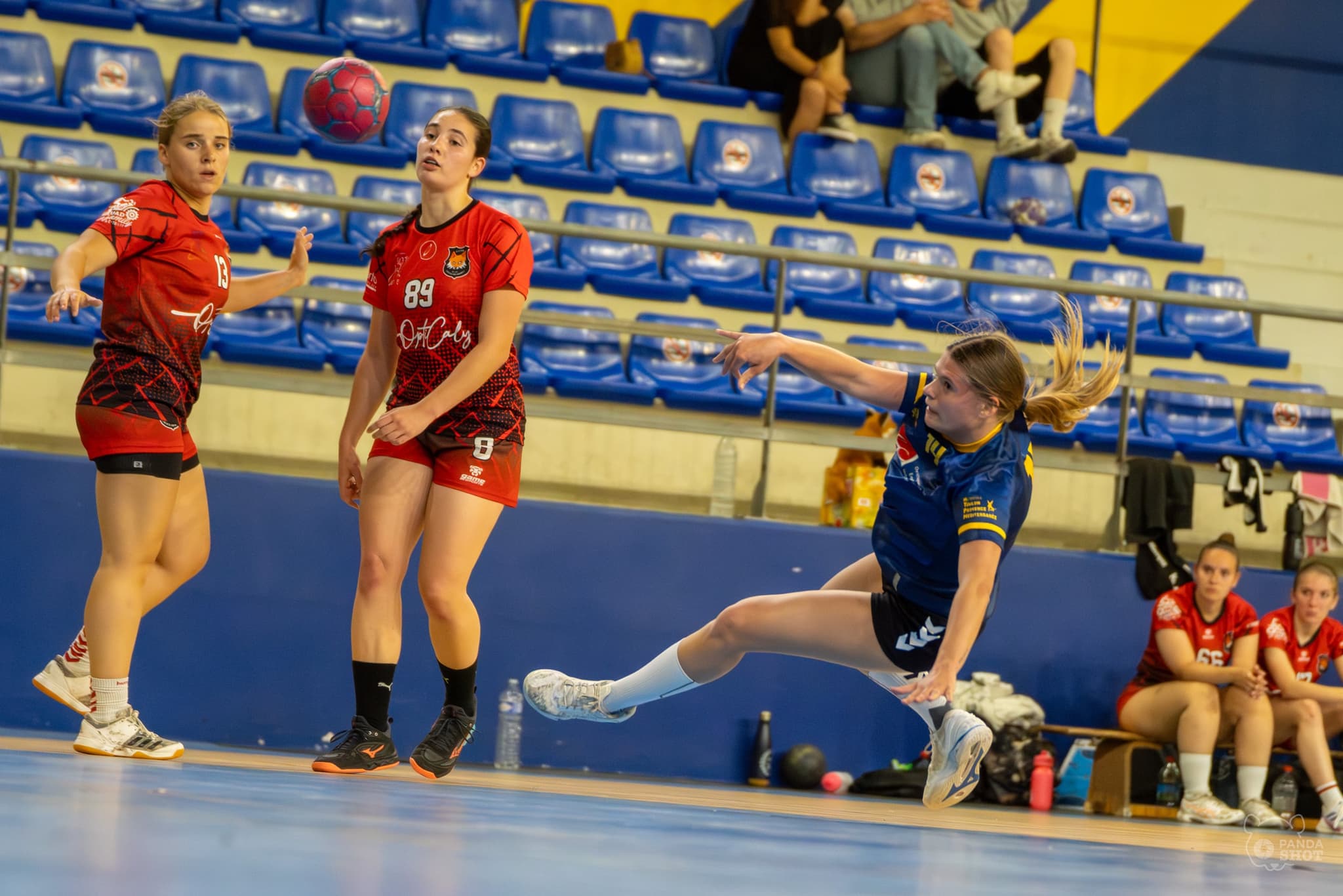 Une jeune handballeuse toulonnaise tire en extension, deux adversaires suivent le ballon des yeux