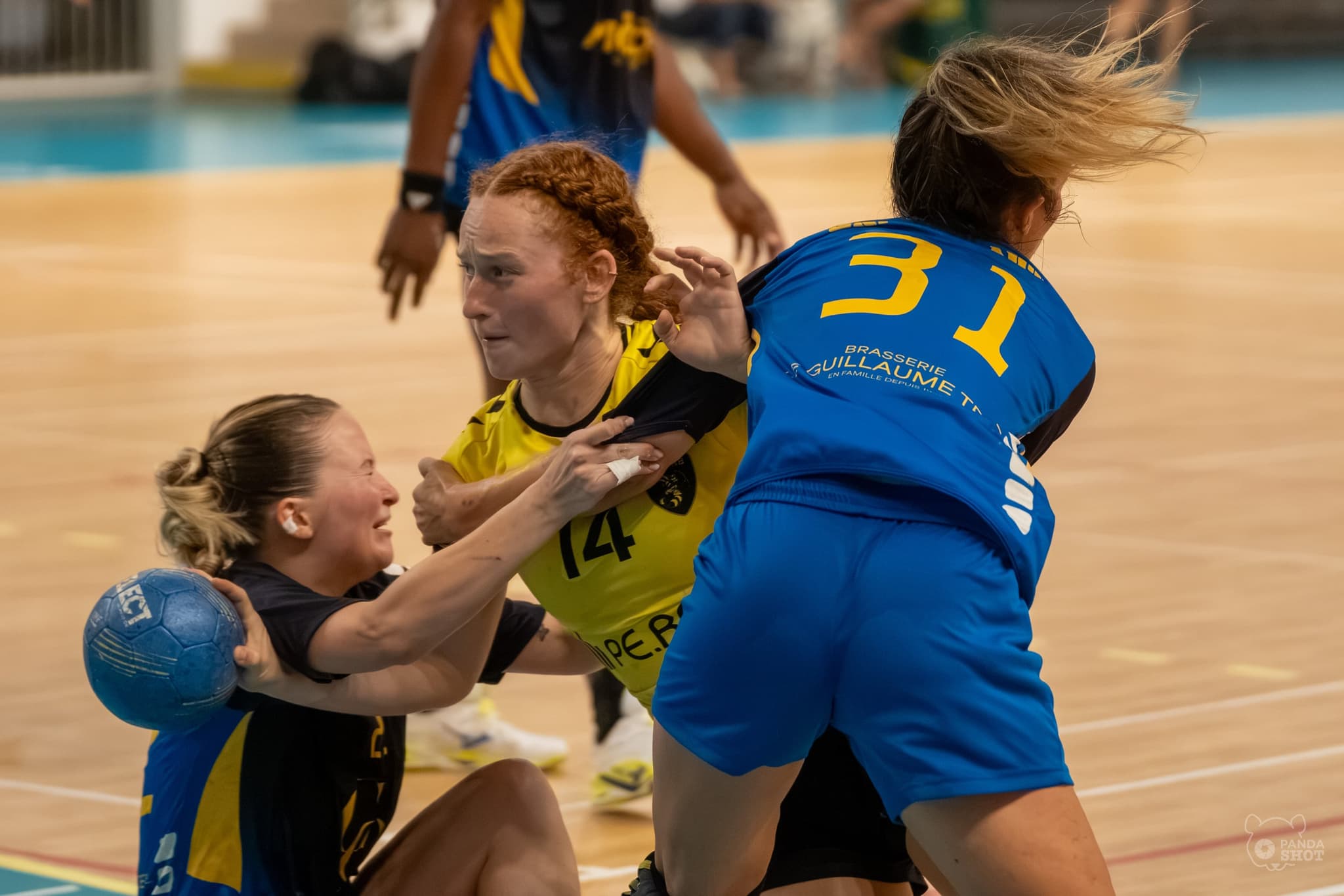Accrochage à trois : une joueuse au sol protège le ballon pendant que deux adversaires la ceinturent
