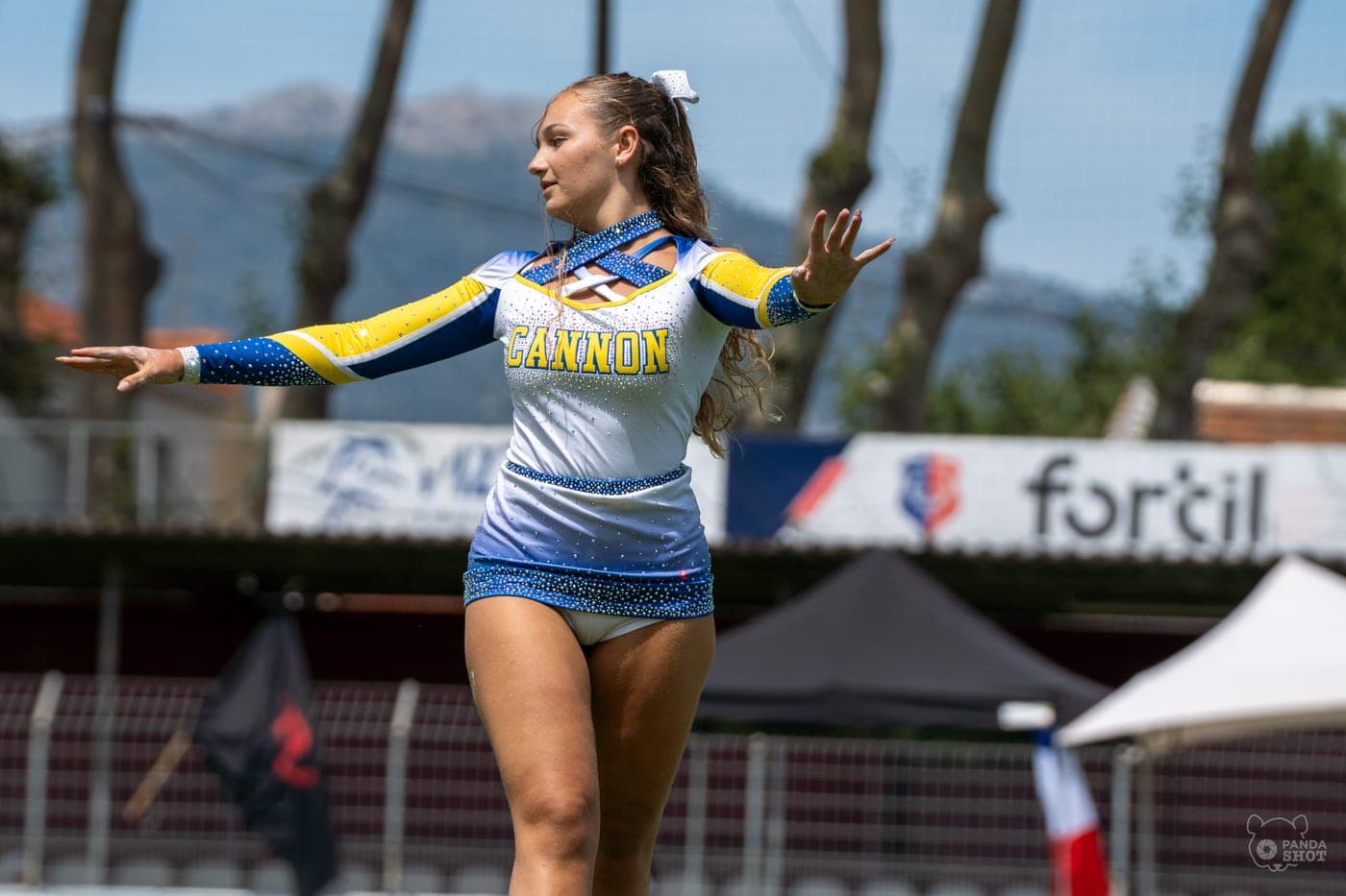 Une cheerleadeuse tient la pose, bras tendus, en compétition.