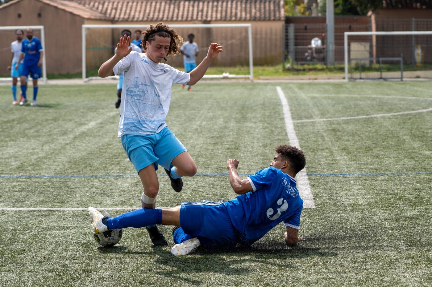 Un joueur célèbre son but tandis qu'un adversaire glisse au sol.